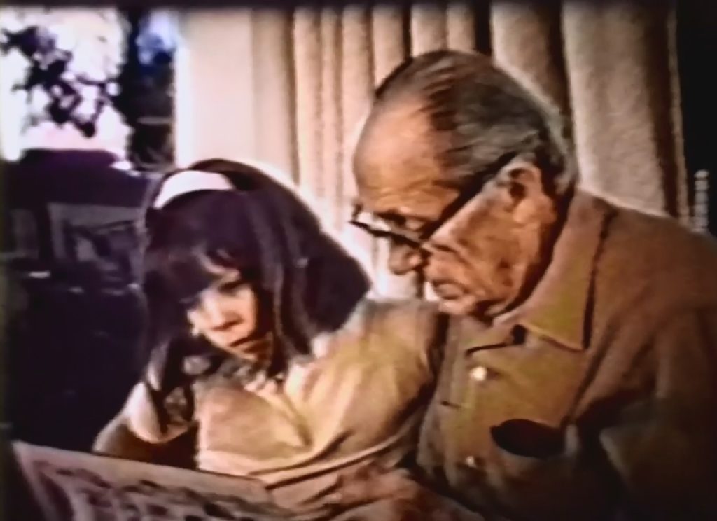 A blurred, upper body shot of an older man and young girl reading a picture book together.