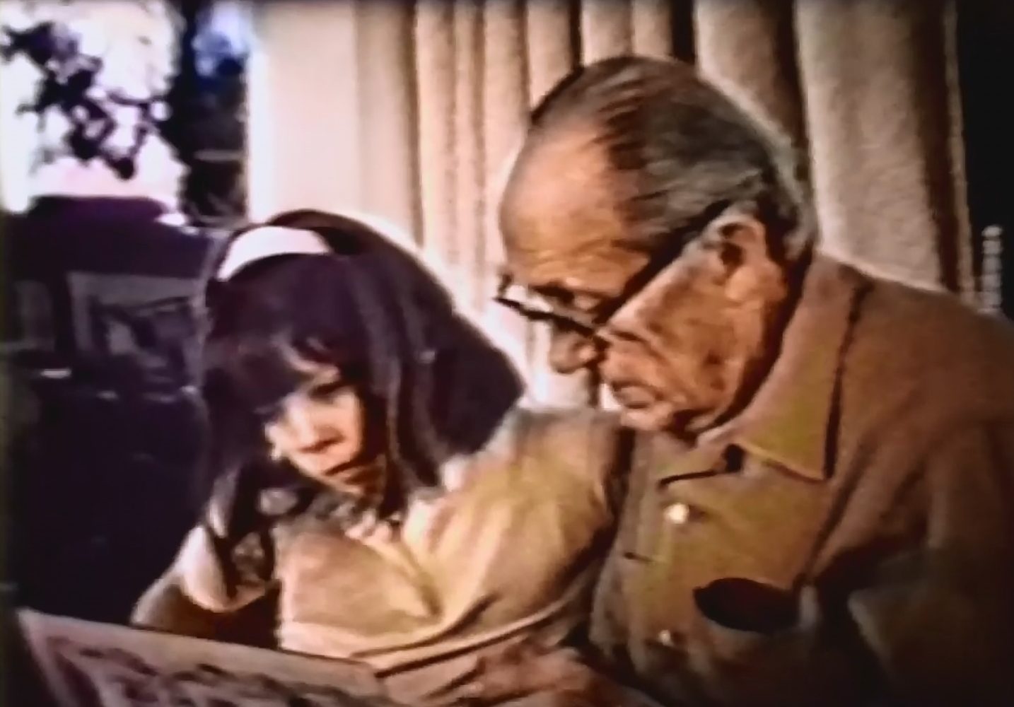 A blurred, upper body shot of an older man and young girl reading a picture book together.